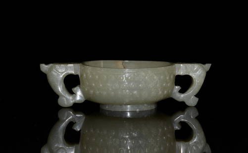 CHINESE QING CELADON JADE TWO-HANDLED CUP: The body is decorated with raised bosses and flanked by two qilin-head handles. Qing period. W. 2.3cm (4 7/8 in.) Provenance: Base has "The British Antique Dealers Association'' sticker. From a privat