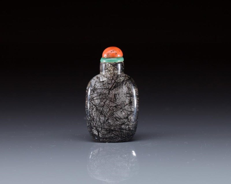 HAIR ROCK CRYSTAL SNUFF BOTTLE: Clear body with black hair inclusions, flask form with a coral stopper, 19th C. H 6.3cm (2 1/2 in.)