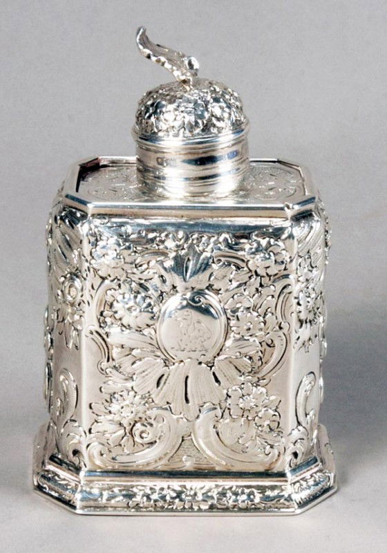 A George I silver canted rectangular tea caddy by: A George I silver canted rectangular tea caddy by John Farnell, London 1715, Britannia standard, the domed pull-off cover with a shell finial, a sliding cover, later chased overall with flowe