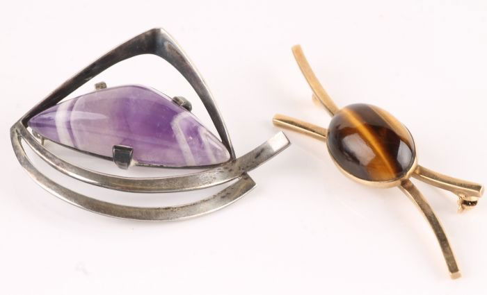 A Birger Haglund tigers eye brooch, stamped 'Haglu: A Birger Haglund tigers eye brooch, stamped 'Haglund' and '9ct', the oval; cabochon set against two curved bars, 6cm long, 7.9g gross; with a 1970's amethyst brooch, stamped 'Sterling' and 'W