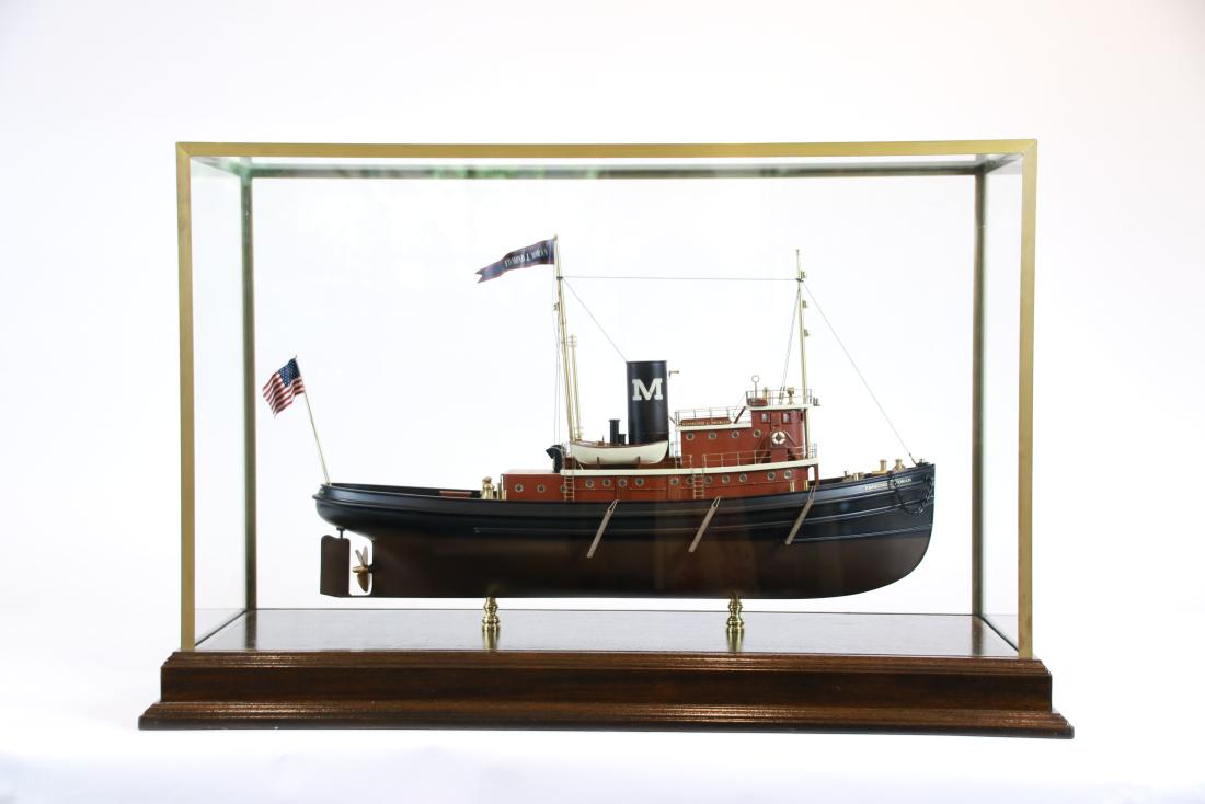 Ship Model of the Tugboat Edmond Moran: Cased model of the New York Harbor Tug Edmond J. Moran. Planked mahogany deck with cabin, wheelhouse, brass masts, winches, bollards, flagstaff etc... A precise scale model. Mounted with brass columns