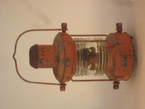 Iron ship's anchor lantern.: Early 20th century ship's lantern in old orange paint with carry and bale handle. Fresnel lens with a few chips. German made. 19 1/2" tall without handle x 9" diameter.