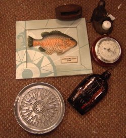 Box lot: Mermaid candle holder, barometer, Caldwell's Rum bottle, small snatch block, compass rose ashtray, and fish plaque.