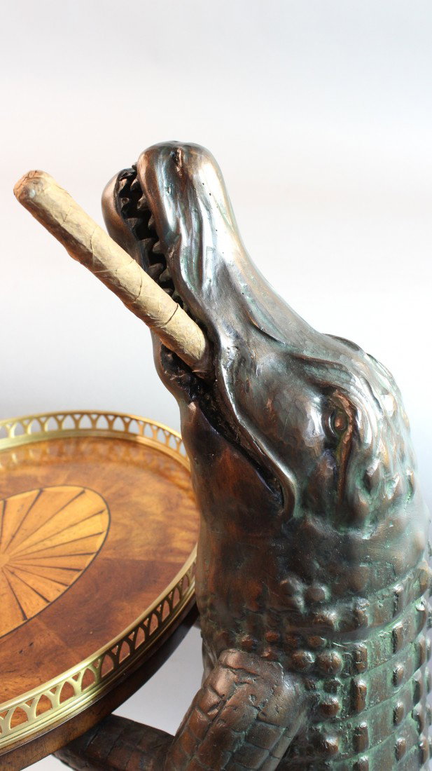 Alligator with cigar hall table: Upright cast alligator with cigar holding a finely executed marquetry inlaid tray with brass gallery. Alligator is standing on a very thick rightly finished wood base with routed edge. 38" x 18" wide.
