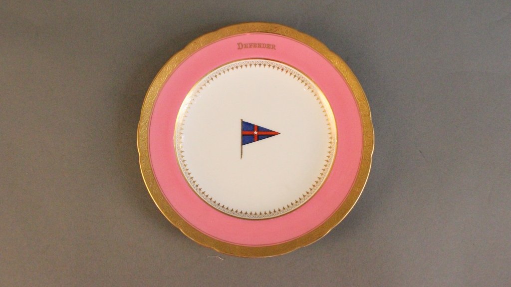 Dish from New York Yacht Club yacht "Defender": Rare, America's Cup collectible, a gold trimmed plate with the New York Yacht Club burgee in the center, yacht name "Defender" gilded on the pink border. Gold leaf border to edge of plate. With maker'