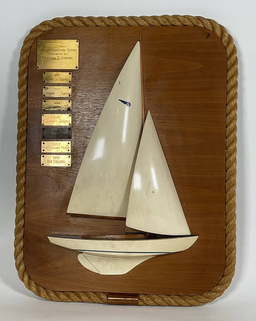 Stillwater Yacht Club Half Model Trophy: Carved half model with carved wood sails. The trophy is for the "Mercury" class one design craft. The blue "M" logo of the Mercury class Yacht Racing Association is on the sail. The Mercury class date