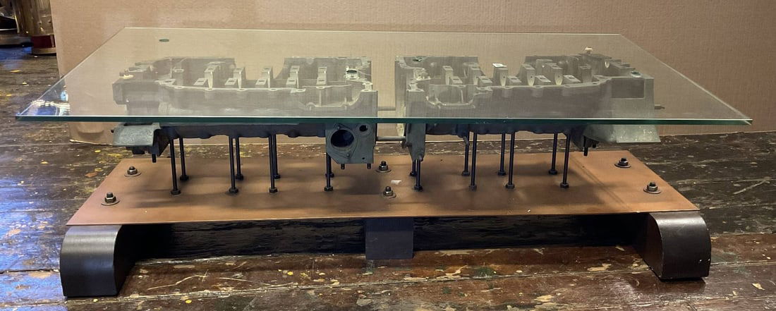 Porsche 911 Engine Block Coffee Table: Coffee table fashioned from a Porsche 911 engine block. Mounted to a base and has a glass top. 48"L x 22" W x 16" T.