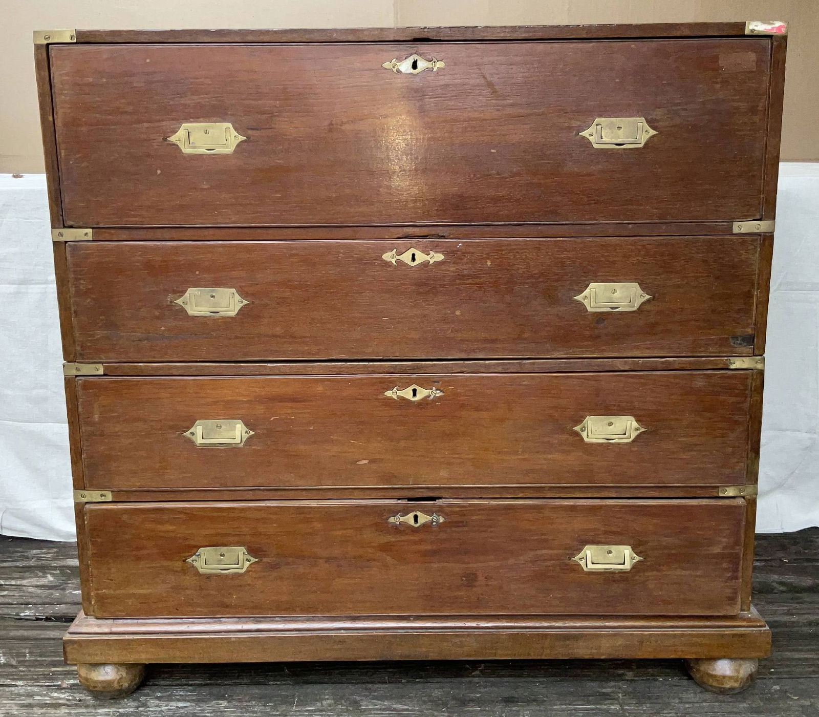 Mid Nineteenth Century Campaign Chest with Brasses: Two-part teak campaign chest with brass corners, handles, keyholes, and bands. Fitted with four bun feet. Top section has a fold down front with desk. Desk has six drawers and cubbyholes. 182 lbs. 44"