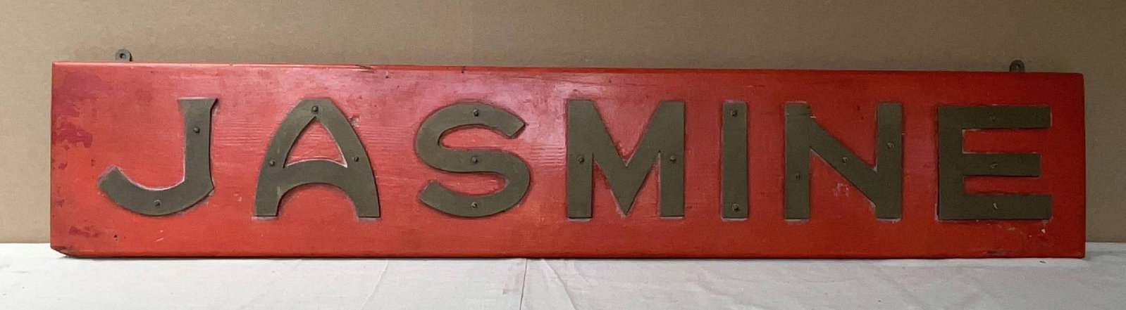Royal Navy Ship's Nameboard from HMS Jasmine: Ship's nameboard from the Royal Navy Flower-class corvette HMS Jasmine. The wood backboard is painted red and fitted with large brass letters. 20 lbs. 10" H x 54" W.