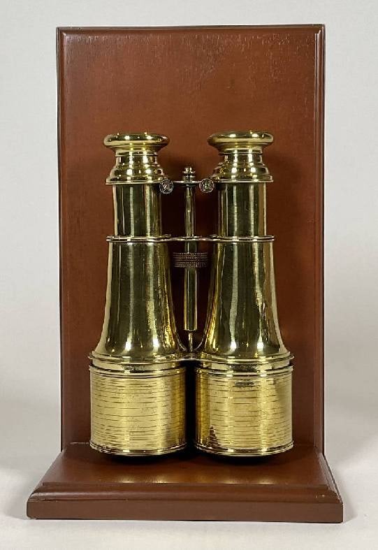 Brass Library Binoculars by Jumelle of Paris: Pair of polished and lacquered early twentieth century yachting or library binoculars by French maker Jumelle. With geared focal knob. Mounted to a mahogany base and backboard. Condition: One small di