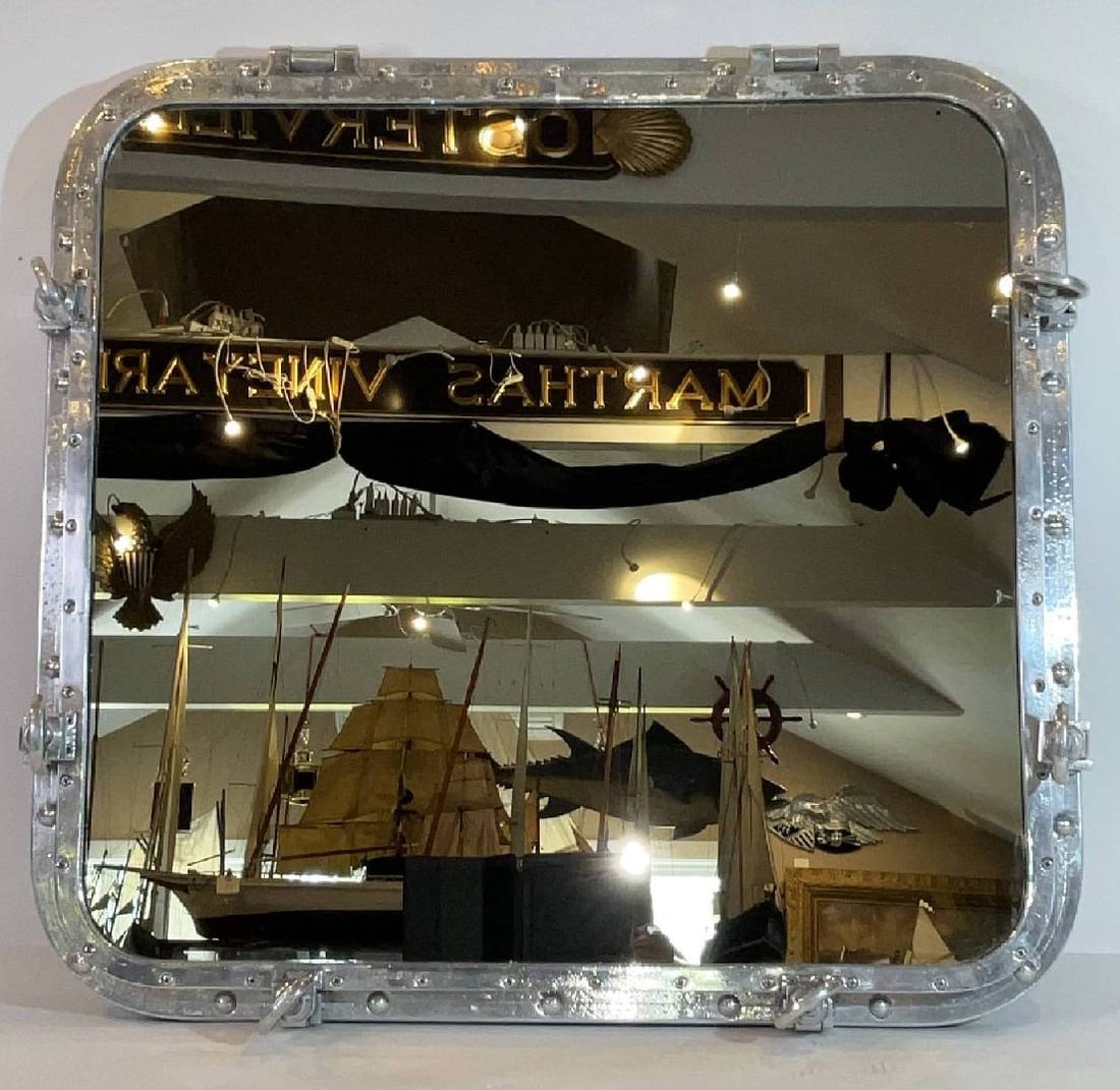 Large Aluminum Porthole Mirror with Wood Back: Polished aluminum porthole mounted to a teak border with a hinged door and six dogbolts. Fitted with a mirror. Great piece of industrial art. 52 lbs. 34"H x 36"W x 6"D.