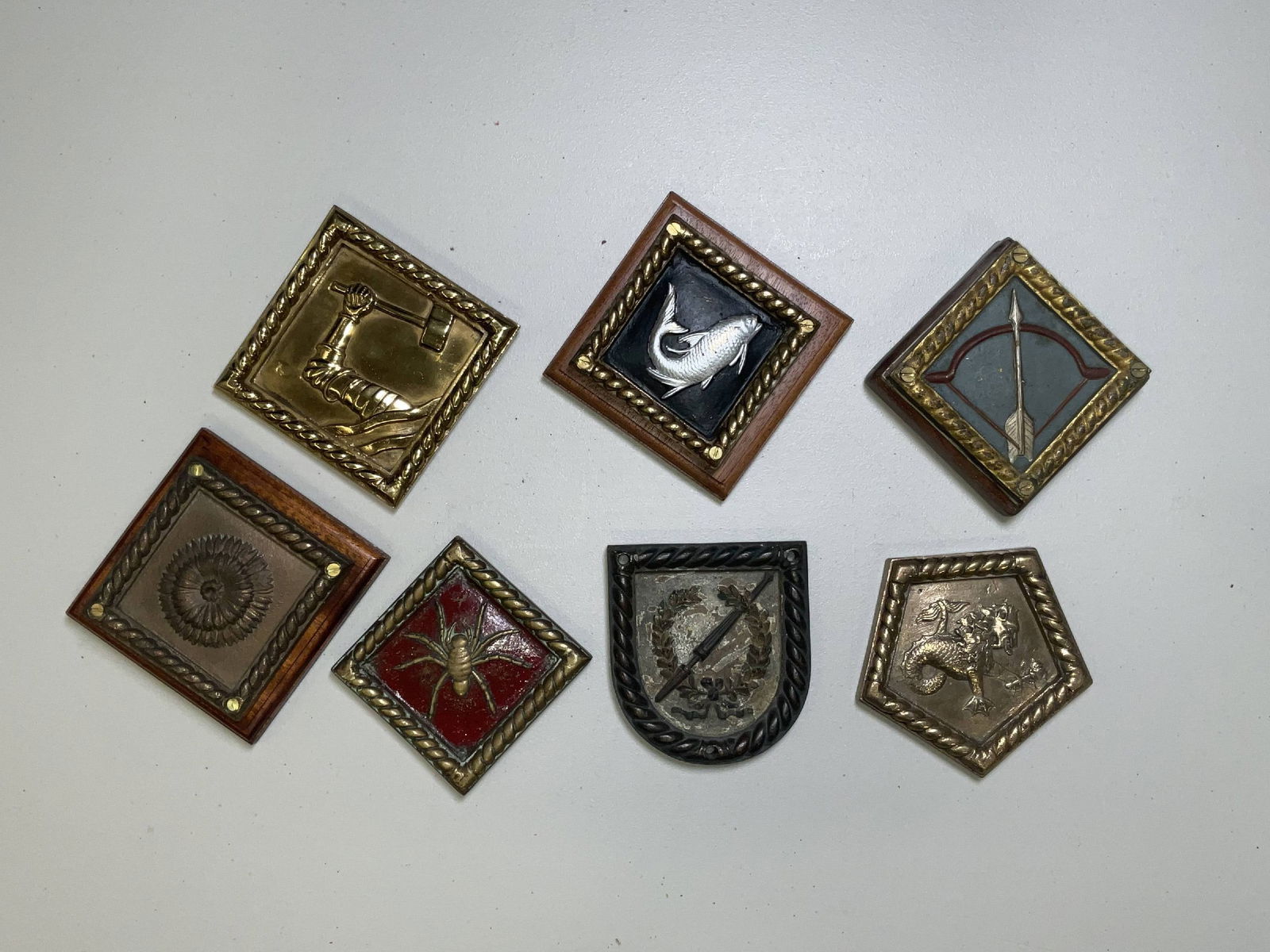 Group of Seven Badges and Tompions From British Royal Navy Ships: A group of seven Royal Navy ship’s badges and plaques, including examples from HMS Tarpon, HMS Sharpshooter, HMS Chrysanthemum, HMS Shakespeare, and HMS Fisgard, among others. Executed in cast