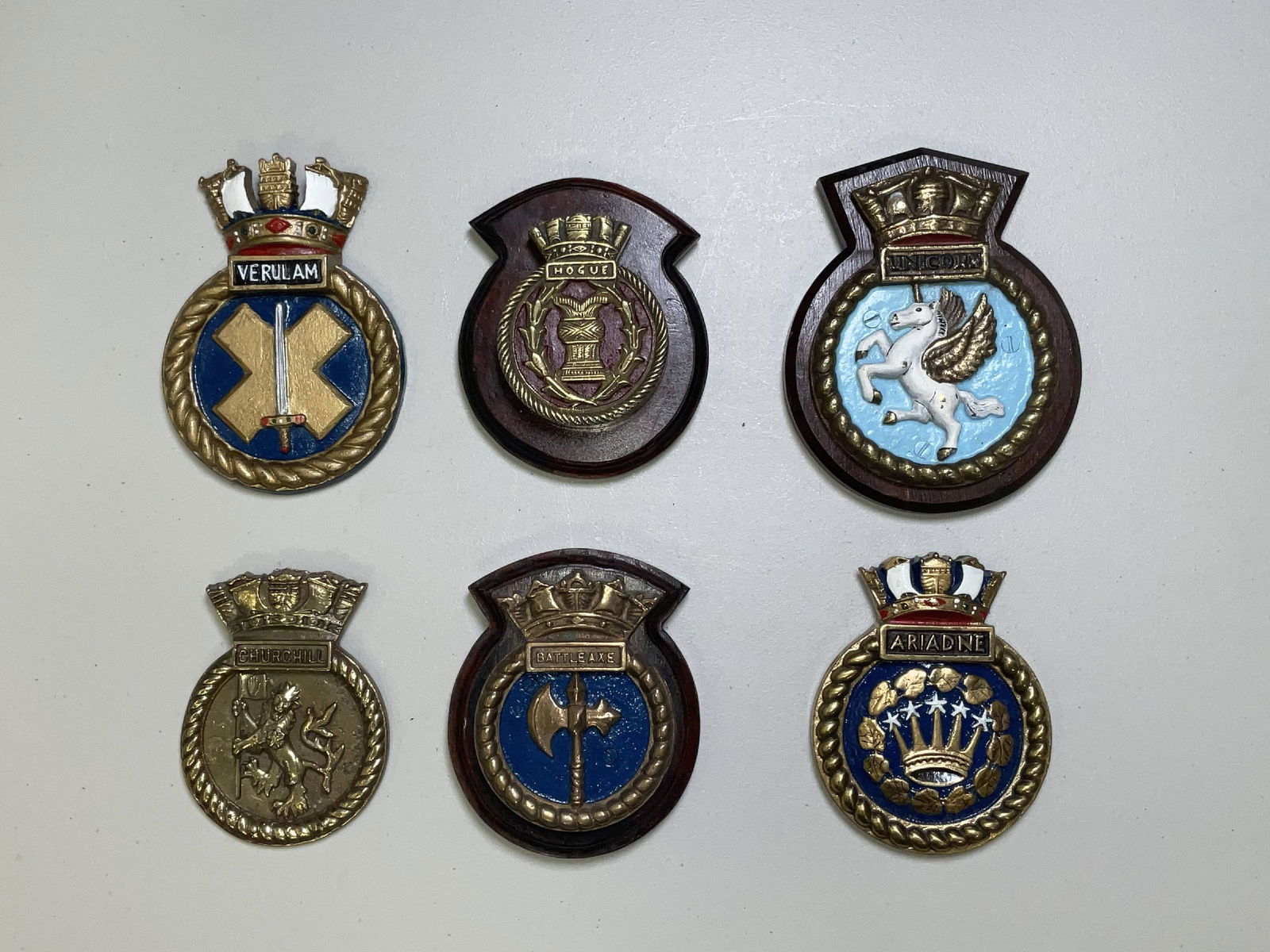 British Royal Navy Ships Badges from Six Warships: Six Royal Navy warship gun tompion crests from HMS Verulam, HMS Hogue, HMS Unicorn, HMS Churchill, HMS Battleaxe, and HMS Ariadne. Nice group of badges from important ships of naval histories. 18 lbs