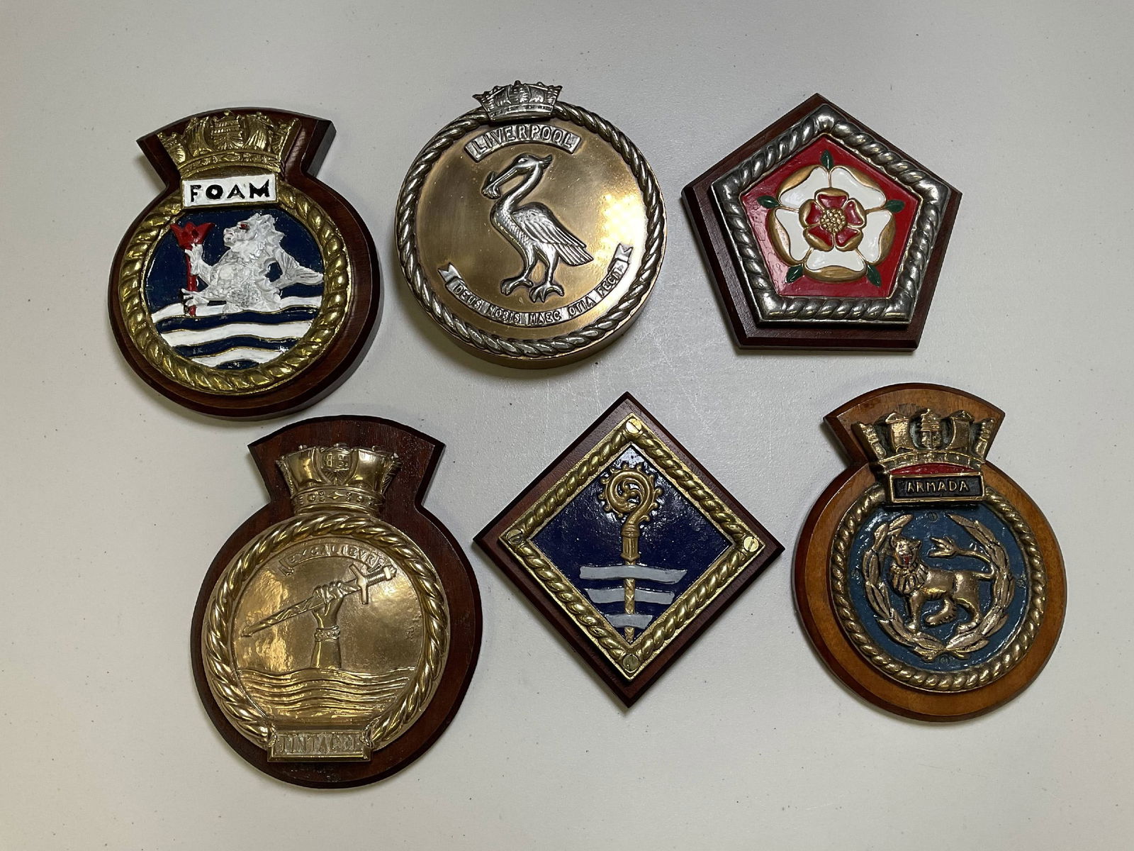 Six British Royal Navy Gun Tompions and Ships’ Badges: Group of Royal Navy badges and a gun tompion from the ocean liner turned navy ship HMS Ambrose, county class cruiser HMS Cumberland, the cruiser HMS Liverpool of 1938, HMS Vengeance, HMS Armada, and