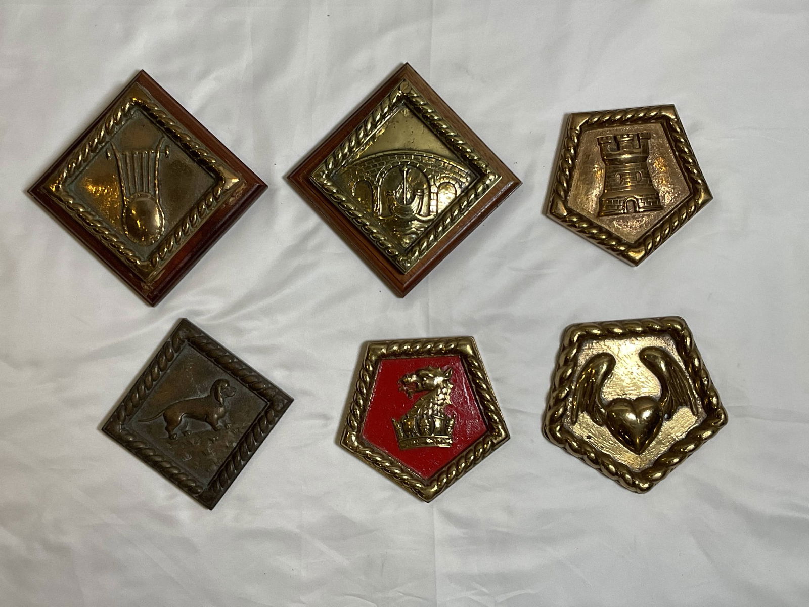 Six Royal Navy Ship's Badges from Various Warships: Group of six badges from HMS Orpheus, HMS Bideford, HMS Newcastle, HMS Basset, HMS Amphion, and HMS Alacrity. HMS Amphion looks like the Ritz-Carlton logo. 6 badges. 15 lbs. 6"H x 6"W big. 5"H x 6"W