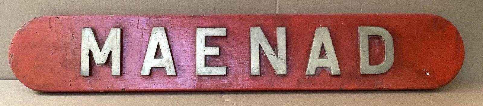 Royal Navy Ship's Nameboard from HMS Maenad 1944: Ship's nameboard from the portside of HMS Maenad, an Algerine class minesweeper built for the Royal Navy during the Second World War. The backboard is painted red with broad brass letters. 20 lbs. 8"