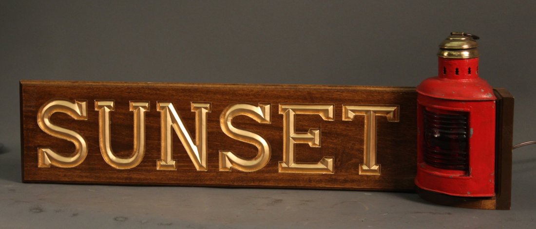 Carved yacht quarter board “Sunset”: A brass topped red port lantern mounted to a deeply carved mahogany yacht name board “Sunset”. 12” x 34”, overall