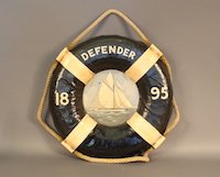 Antique Cork Yacht Lifering: Antique canvas covered cork life ring with rope handles fitted with a wood panel with portrait of the America’s Cup yacht Defender of 1895. Artwork is not antique. Diameter of life ring is 18”.
