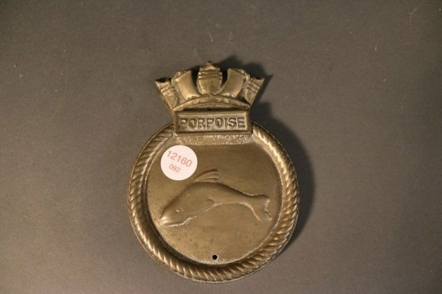 Heavy Brass Badge from "Porpoise": Heavy ship's badge of brass showing a porpoise and crown. Dimensions: 6.5" L x 5" H *This lot is part of a maritime antique auction of ship models, nautical relics, marine paintings, boat parts, yacht