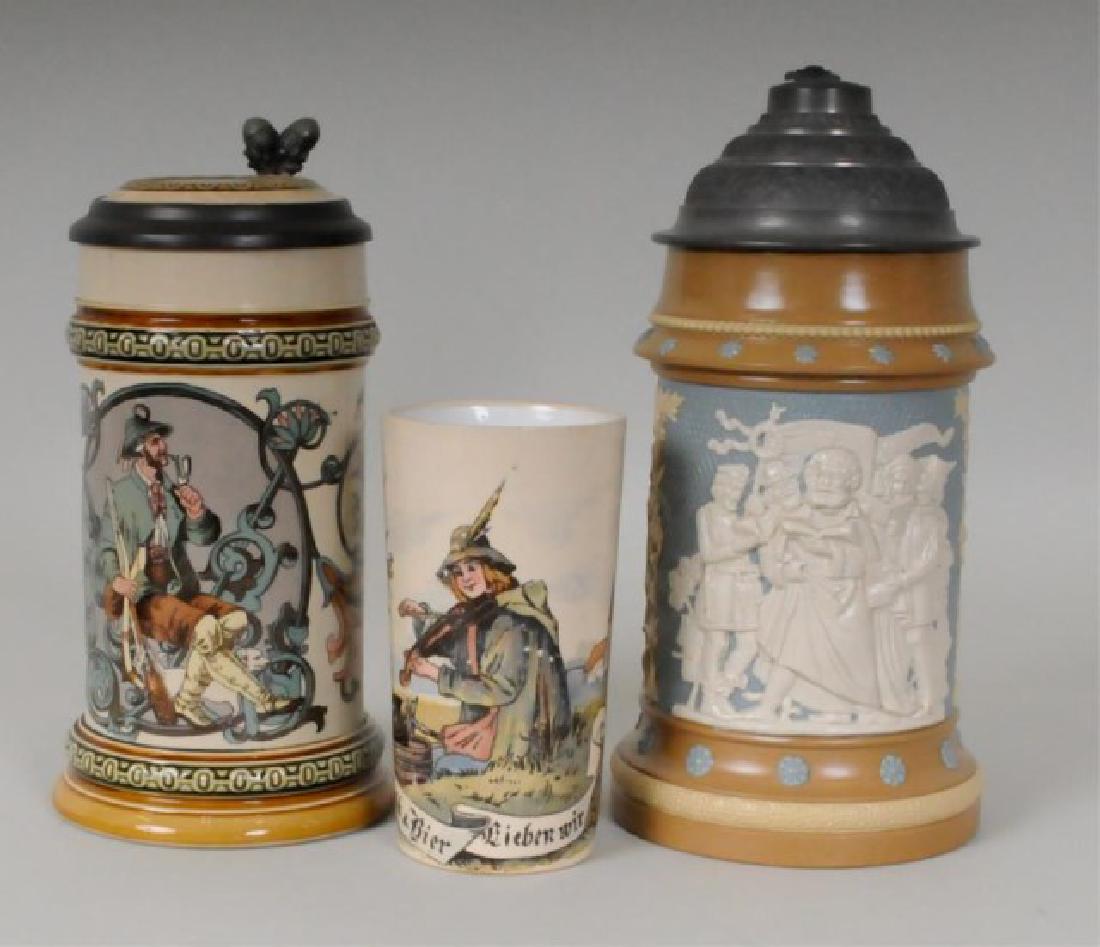 Mettlach Steins & Beaker, 3 Pieces: 1. 1/2 liter relief stein, No. 202, group of men singing on a blue background, pewter lid and thumbpiece; marked on base; 9"H; firing flaws to rim---2. 1/2 liter PUG stein, No. 580(1530), hunter smoki