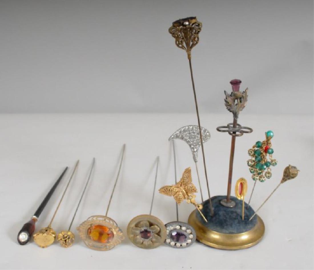 Brass Hatpin Holder & 12 Pins: Brass hatpin holder having an amethyst faceted glass acorn finial with oak leaves, circular base; 3" bottom dia., 6 1/8"H---Twelve hatpins and stick pins including one Miriam Haskell with butterfly an