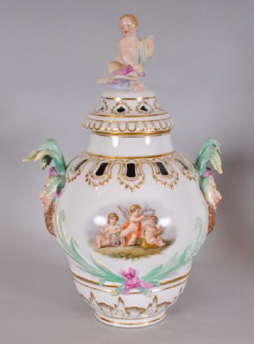 KPM Porcelain Covered Urn w/ Jester Masks: Porcelain KPM potpourri urn or covered vase, pierced lid with finial designed as putto holding a bird; pierced vase painted with three putti on one side, floral bouquet on other, and floral and foliat