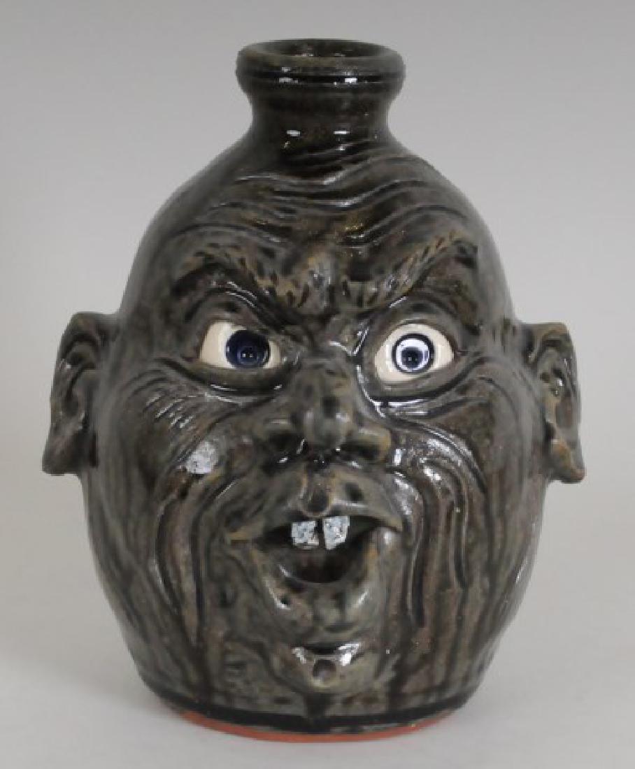 Dwayne Crocker, Georgia Stoneware Face Jug: Dark to light olive runny alkaline glaze, expressive face having open mouth with two teeth above a cleft or dimpled chin, signed on base "Dwayne L. Crocker / Gillsville Ga. / 6-29-2001"; 7"H; good con