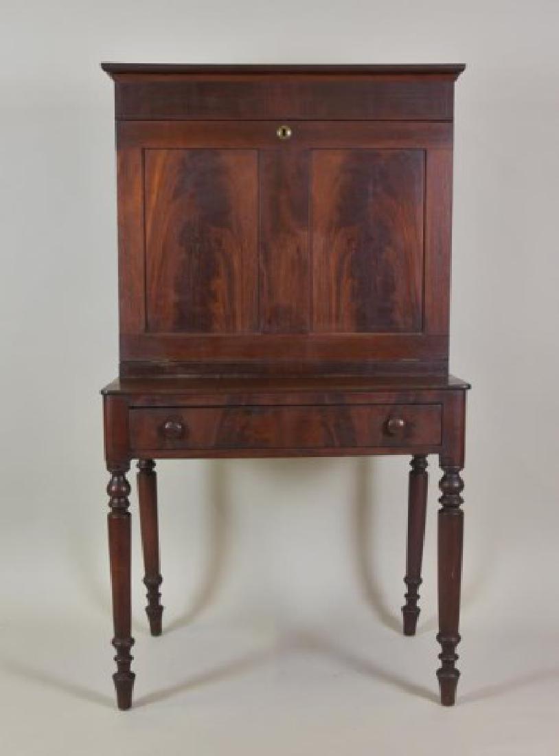 American Mahogany Plantation Desk: Mid 19th century, cornice having a hinged rectangular top lifting to reveal hidden storage compartment; door with flame mahogany paneled front lowers to reveal interior with two dovetailed drawers, cu