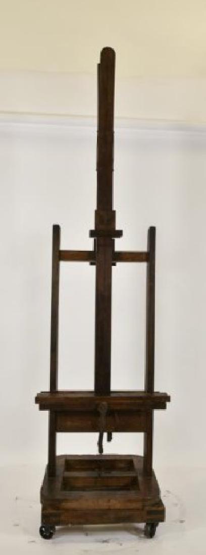 19th Century Double Sided Artist's Easel: Double sided wood easel with swivel base, crank with wooden handle for adjusting height by screw and gear mechanism, two upright supports with mortise and tenon construction, on metal casters; 27 1/2"
