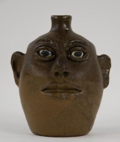 Lanier Meaders Face Jug: White County, Georgia, 1917-1998; flat matte glaze, applied facial features, white clay eyes with blue/black pupils, applied strap handle, signed on base "Lanier Meaders"; 9"H; crack to base of handle