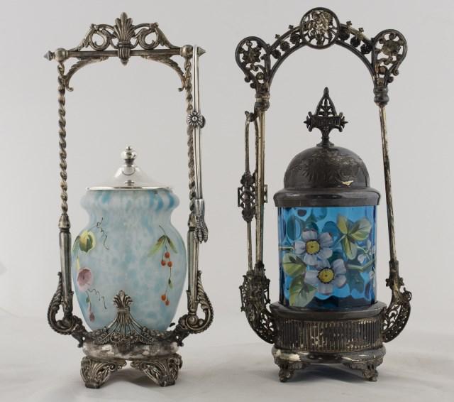 Two Enameled Art Glass Pickle Castors: 1. Blue inverted thumbprint art glass jar decorated with polychrome enamel flowering branches, in E. G. Webster & Son quadruple plate stand, with decorative domed lid and tongs; overall 12"H, jar 4 3/
