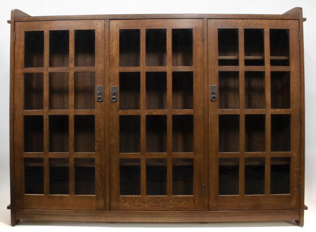 Stickley Audi Arts & Crafts Style Oak Bookcase: No. 89-647, triple bookcase, each door with twelve individual panes of glass, interior with fixed middle shelf and adjustable shelves on top and bottom, dark copper hardware, branded mark and metal ta