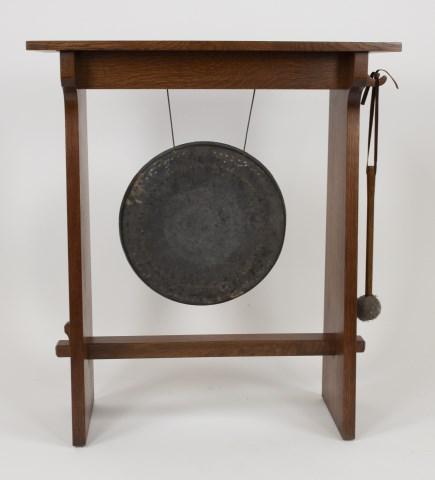 Stickley Audi Arts & Crafts Style Oak Dinner Gong: No. 89-812, hand-hammered bronze gong in oak stand supported by oak keyed through tenons, with striker, branded mark and metal tag; 31"W, 12"D, 36"H; good condition with minor abrasions commensurate w