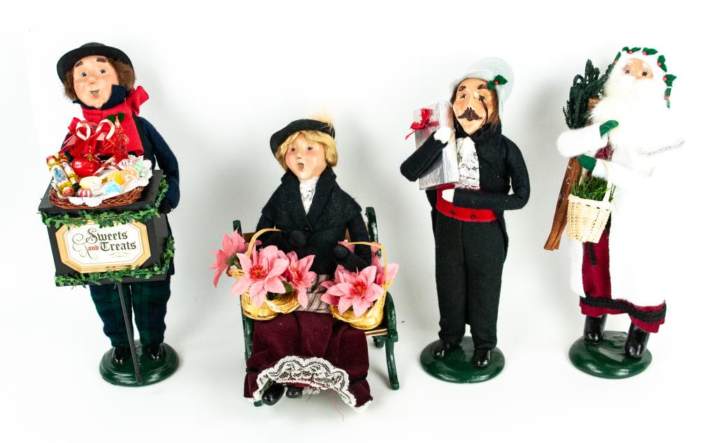 Four Byers Choice Christmas Carolers: 2007 male with "Sweets and Treats"---1988 male holding silver package---1987 male with white beard carrying sticks and a basket of greenery---2000 female sitting on a wood and metal bench, holding two