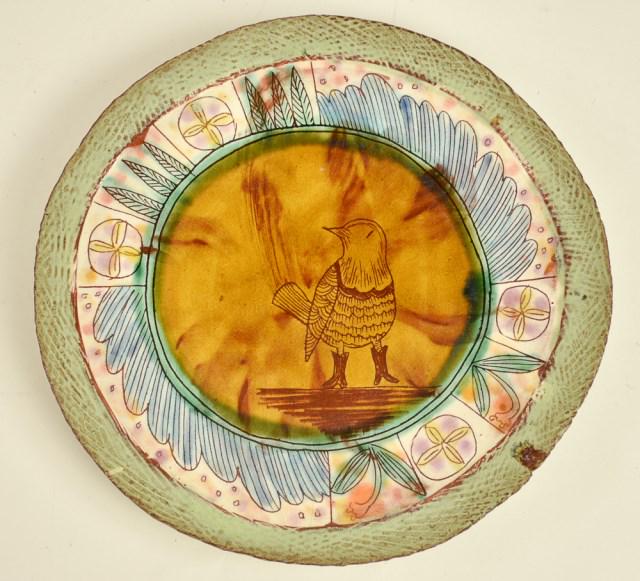 Shoko Teruyama (Japanese/American): Whimsical earthenware plate with white slip and sgraffito decoration featuring a bird wearing boots at center surrounded by a border of feather panels alternating with foliate and floral panels, green