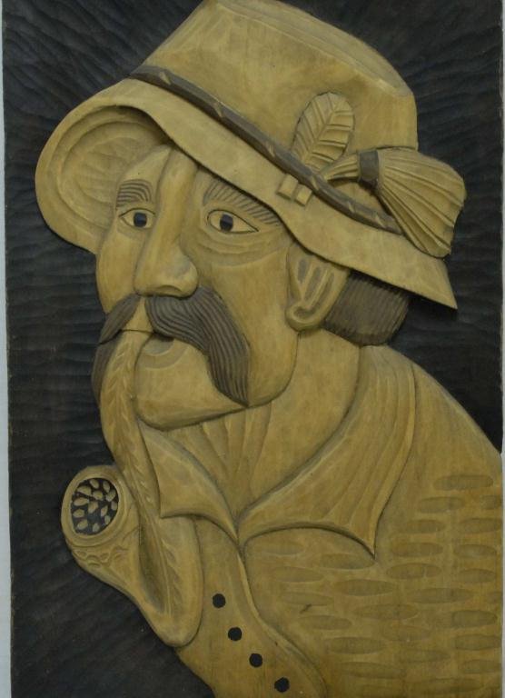 Folk Art Hand Carved Wood Portrait of Man Folk art : Folk Art Hand Carved Wood Portrait of Man Folk art hand carved wood portrait of older mustached man wearing hat and smoking a pipe; natural wood with stain decoration; 12 3/4"W, 21 1/4"H, 1 1/4"D
