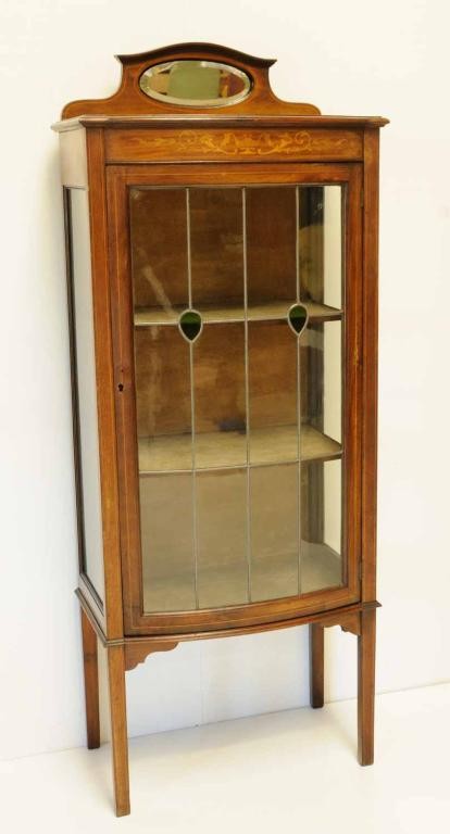 Edwardian Inlaid Curio Cabinet: Mahogany with satinwood banding; foliate inlaid frieze; crest with oval beveled mirror; glass sides and leaded glass door set with two green textured glass accents of teardrop form opening to a fabric