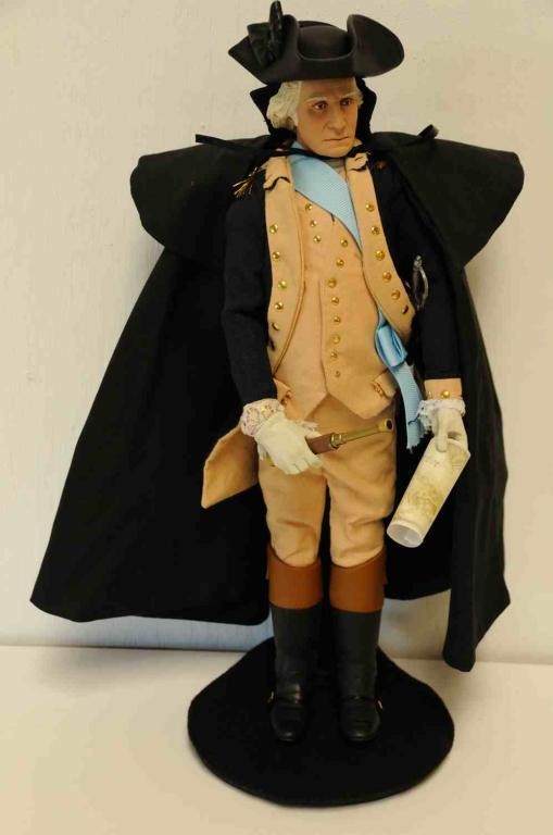 George Washington Doll: Dressed in cloth fabric cape with overcoat featuring Rank Star, tailcoat, vest, breeches, stockings, baldrick; wearing a tricorn hat and boots; telescope, sword hanger with scabbard, English spurs, ma