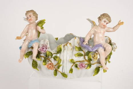 C. G. Schierholz & Sohn Porcelain Center Bowl: German porcelain bowl of oval form with applied leaves and flowers, a full-figure winged cherub sits on each front corner, underside marked with blue underglaze double crossed swords and incised "Germ