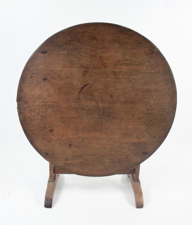 Folding French Provincial Wine Tasting Table: Early 19th century, oak wine tasting table (table de vigneron), round tilt top with banded edge above a carved swing support, trestle base with stretcher and shoe feet; 39" dia., 27 3/4"H, 45"H folded