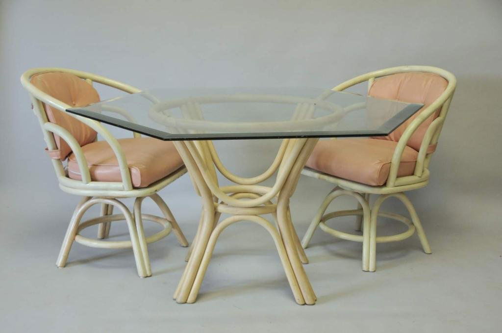Rattan Glass Top Table w/ Two Chairs: Table with painted rattan base and hexagonal beveled glass top; 55 1/2"W, 28 1/2"H; two swivel painted rattan chairs with loose back and seat cushions; 24"W, 25"D, 31 3/4"H; some chipping to paint on