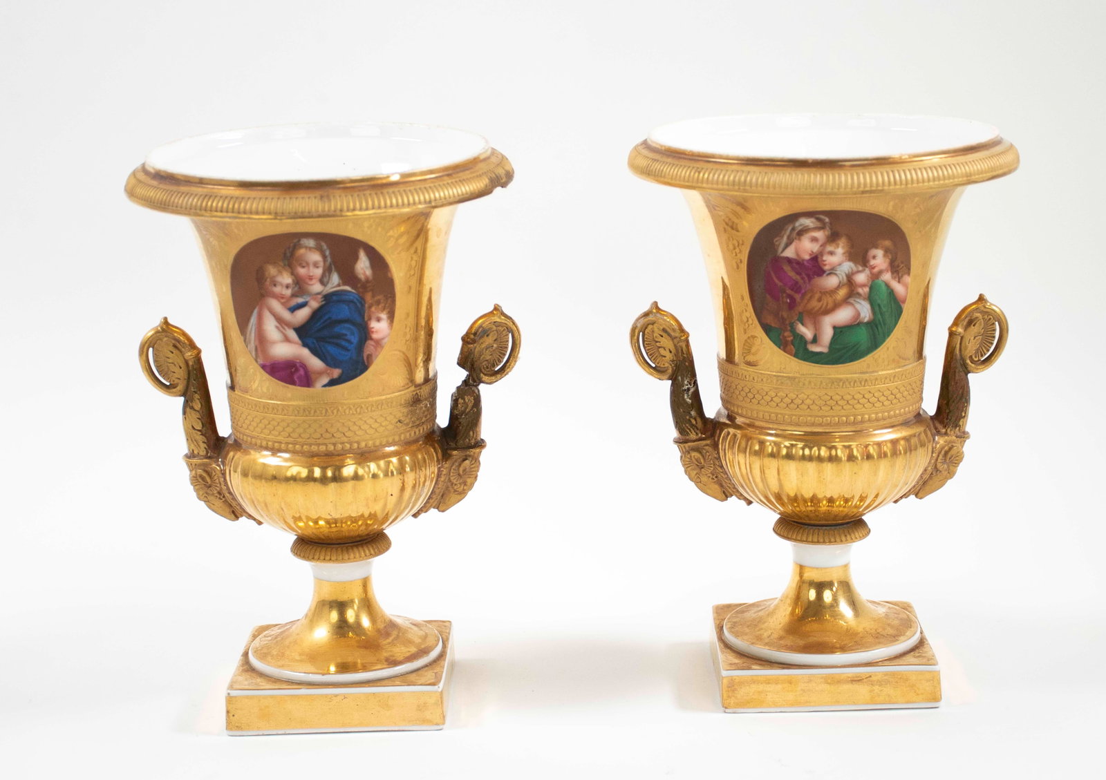 Pair of Old Paris Porcelain Vases: Pair of gilded porcelain urrn form vases with double handles, each with a varying hand painted polychrome reserve of the Madonna and Child with an onlooking angel, reverse with gilded design of