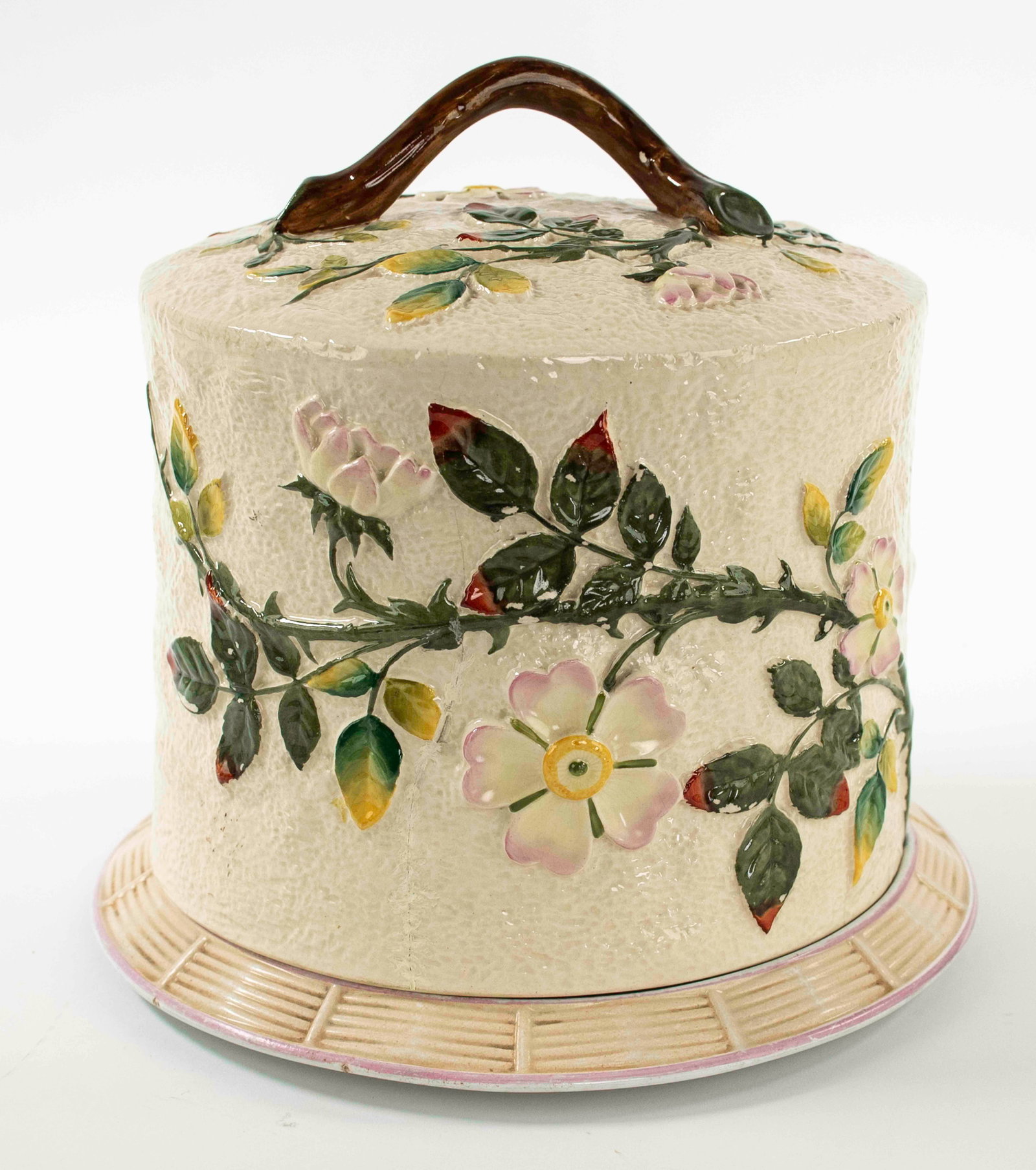 Majolica Ceramic Cheese Dome on Tray: Cheese dome decorated with trailing thorny vines and flowers in relief on a textured cream ground, twig form handle, resting on a tray with basket weave rim, base of tray incised "E K D"; tray 11" dia