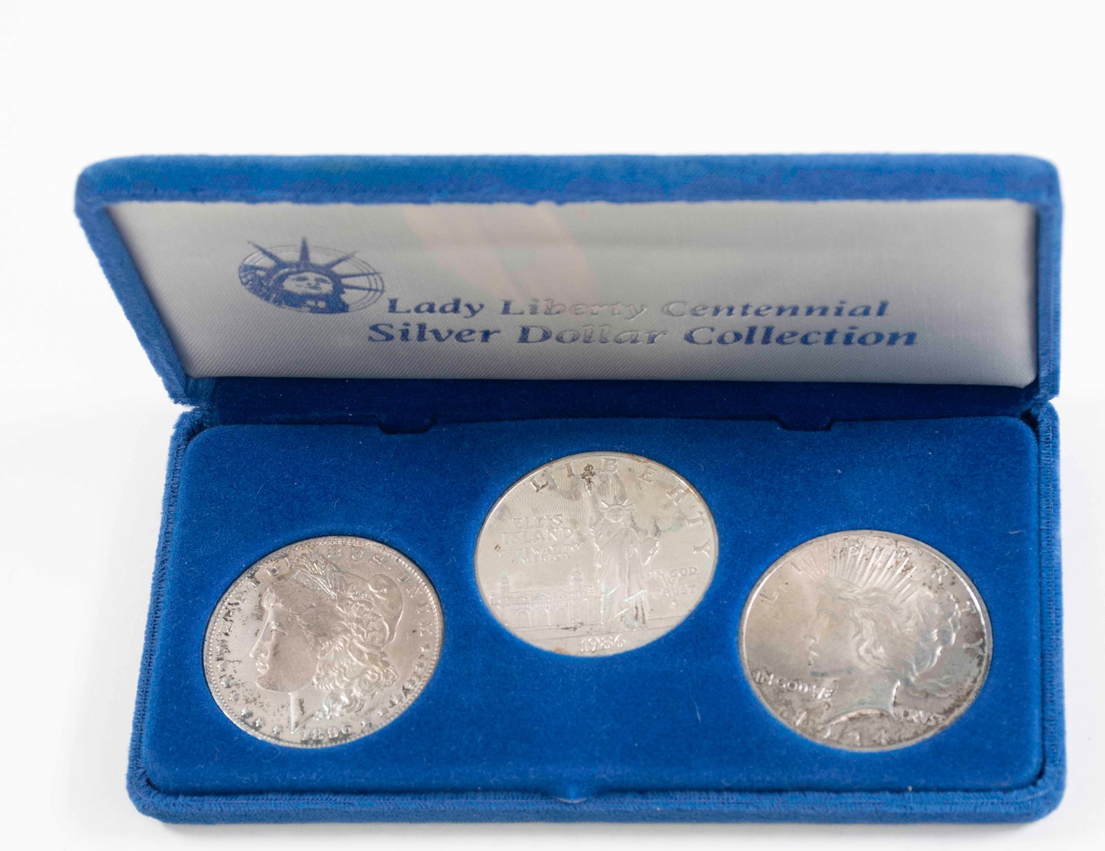 Morgan, Peace, Ellis Island Silver Dollars: 1924 Peace Silver Dollar, 1896 Morgan Silver Dollar, 1986 Ellis Island Silver Dollar in blue velvet case "Lady Liberty Centennial Silver Dollar Collection" with COA