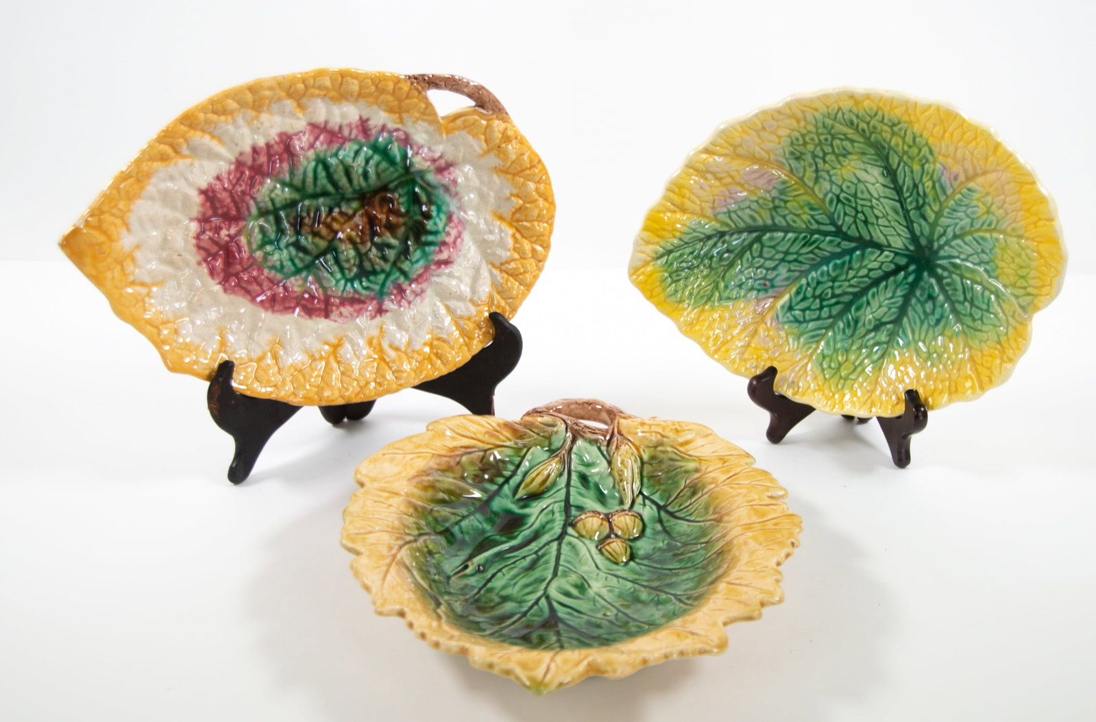 Three Majolica Leaf Form Bread Trays: Qualifies for in-house shipping---1. Begonia leaf with a pink, green and yellow glaze; twig handle; 11 1/2" x 7 7/8", 1 1/2"H---2. Oak leaf and acorns with twig handle; green, yellow and brown glaze; 
