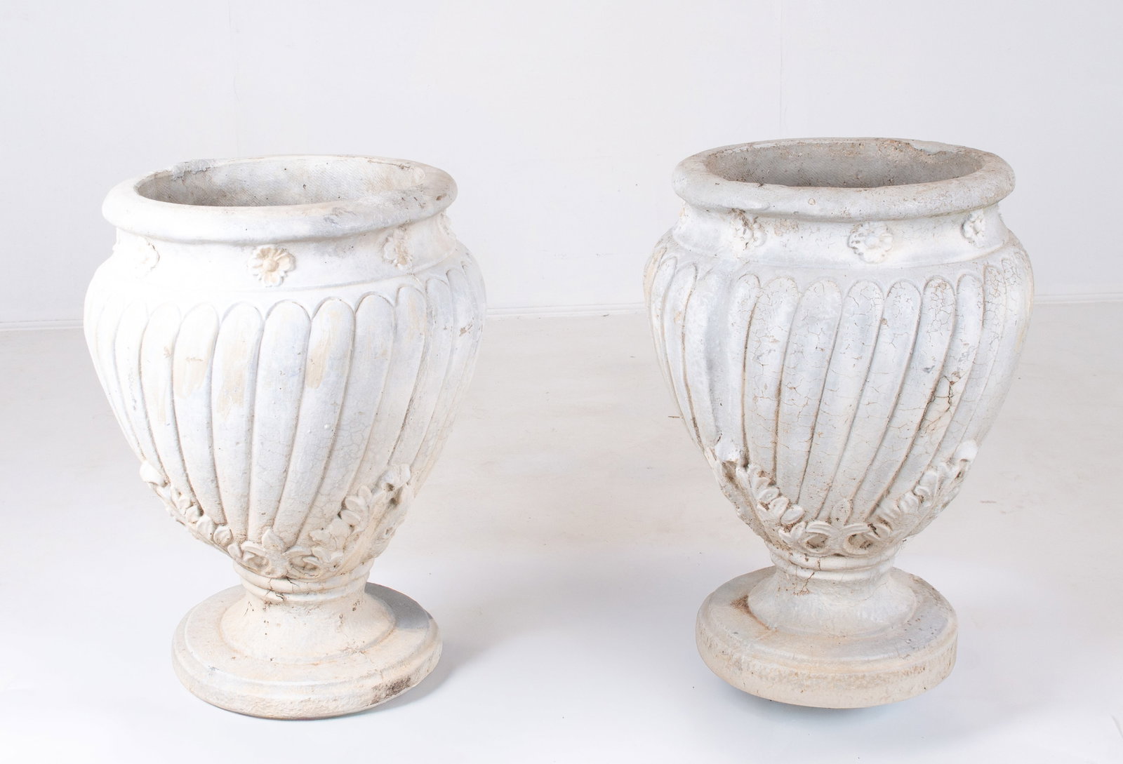 Pair of Concrete French Style Garden Urns: Each having a band of floral medallions below rim over a ribbed body with molded acanthus leaves alternating with fleurs-de-lis near base, stepped round foot; approx. 23 1/2"H, 15" top dia.; good