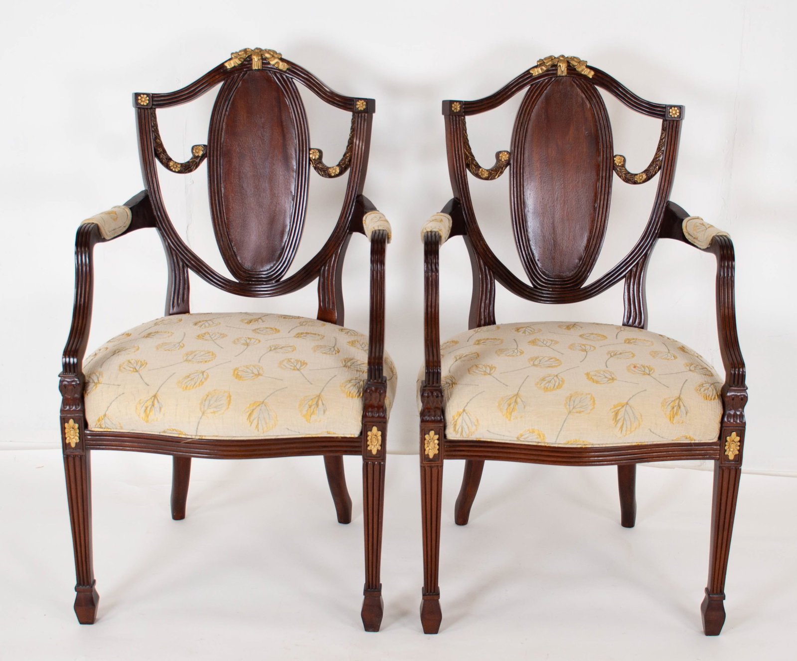 Pr. Mahogany Shield Back Armchairs: Each having an arched crest with carved gilt ribbon and bow at center and terminating in gilt floral medallions, shield back flanked by carved floral swags with gilt accents, neutral floral upholstery