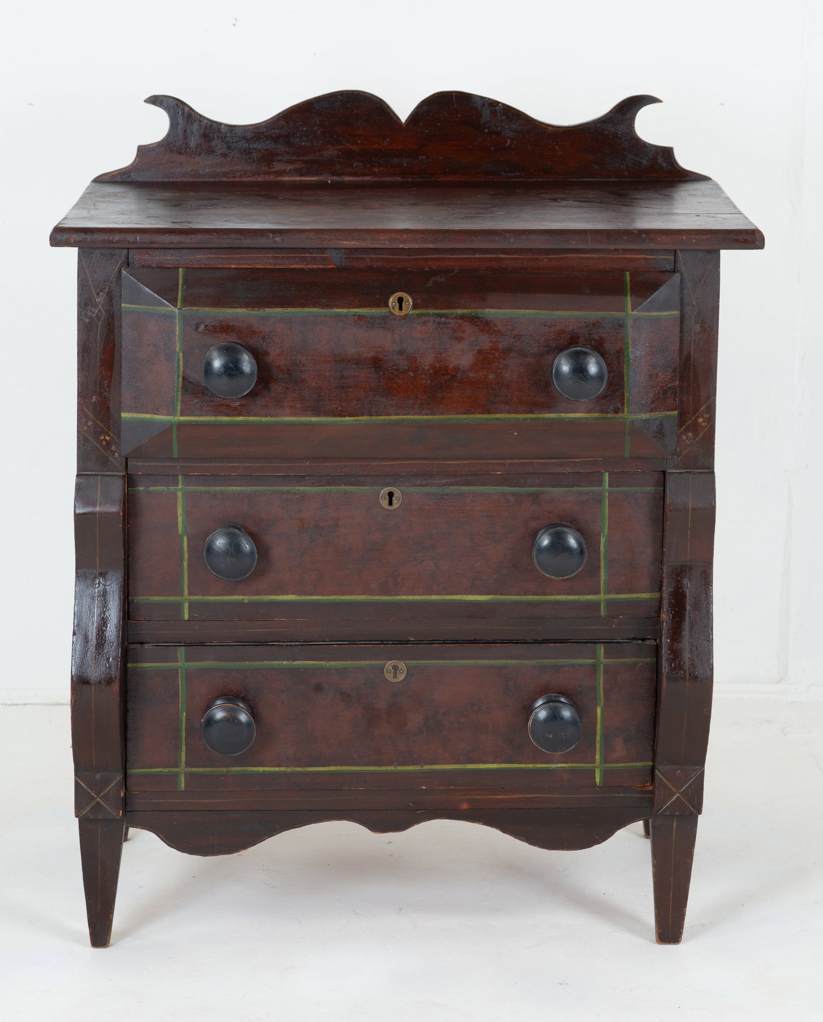Am. Diminutive Grain Painted & Stenciled Chest: 19th century; rectangular top with applied scalloped backsplash; slightly projecting top drawer having boldly beveled edges, over two lower drawers flanked by scrolled stiles; paneled sides; square ta