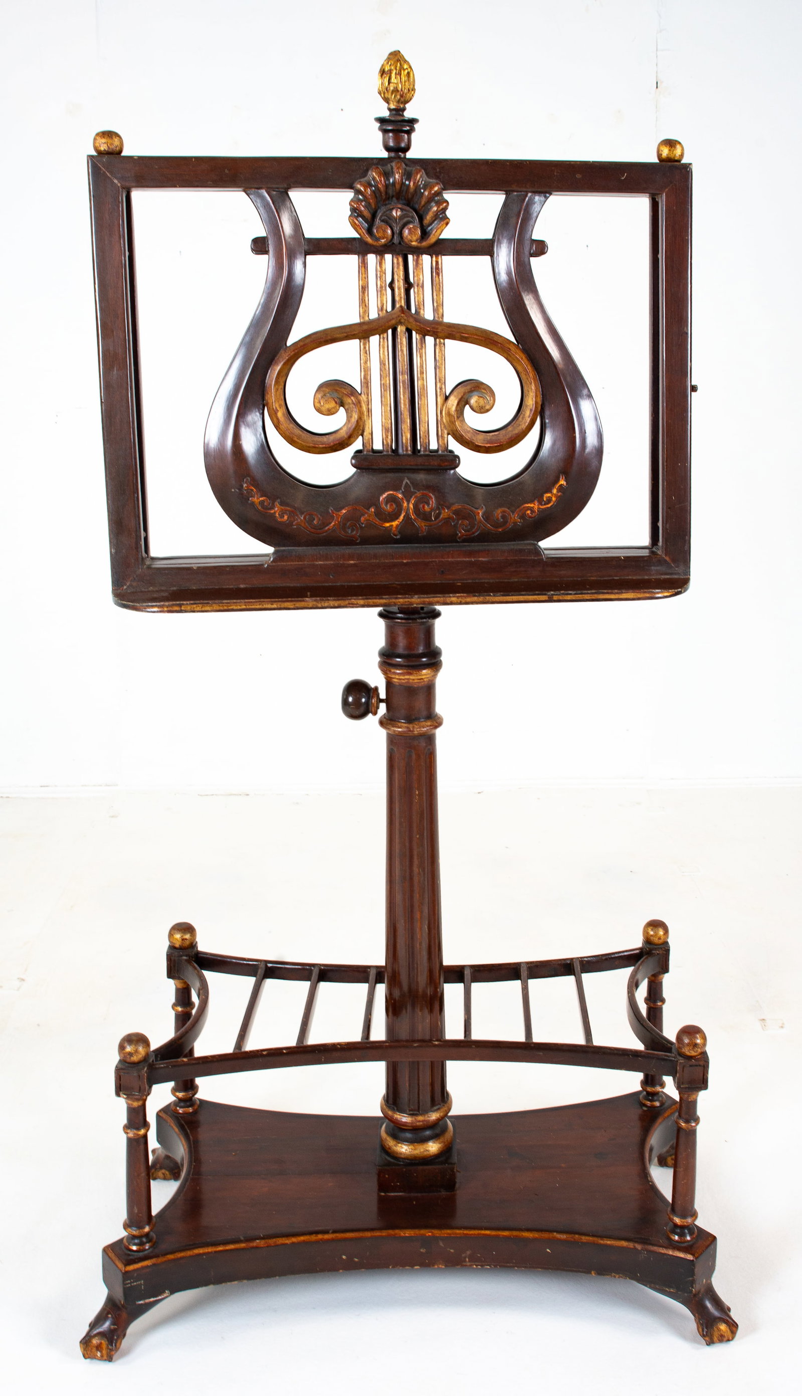 Double Sided Mahogany Parcel Gilt Music Stand: Ratcheted double lyre-form top with flame finial, adjustable telescoping fluted stand, quatrefoil base with dividers for music, ball and claw feet; 28"W, 14 1/2"D at base, 54"H - 69"H; double sides