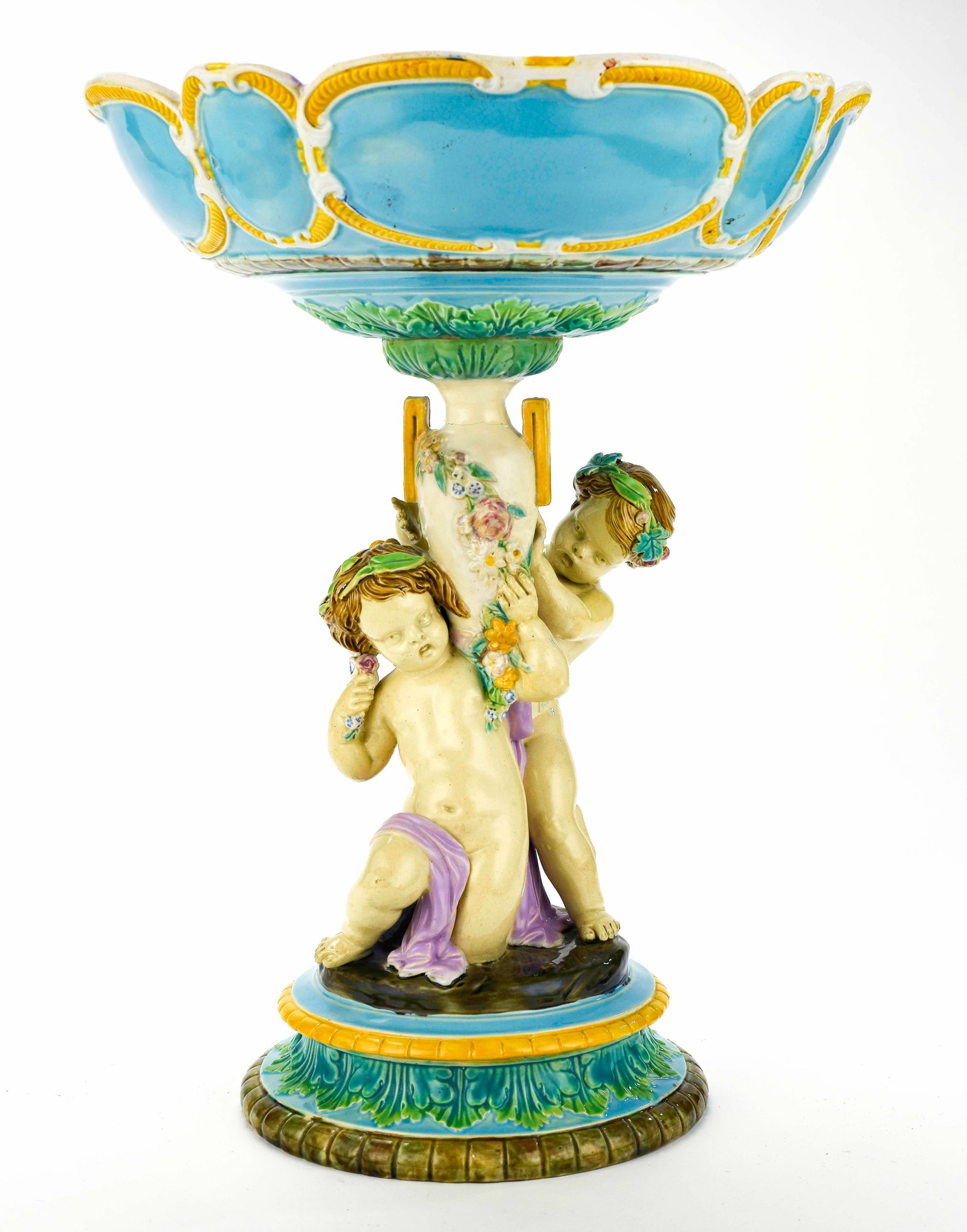 George Jones Majolica Figural Comport Centerpiece: Qualifies for in-house shipping---Bowl having lilac interior and exterior with turquoise cartouches trimmed in white and ochre, bowl supported by two putti, stepped round base with foliate